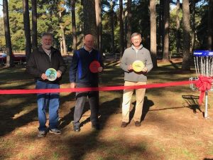 Three men holding discs during the ribbon cutting of the disc golf course